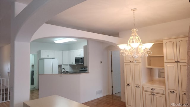 kitchen featuring pendant lighting, light hardwood / wood-style flooring, stainless steel appliances, white cabinets, and a chandelier