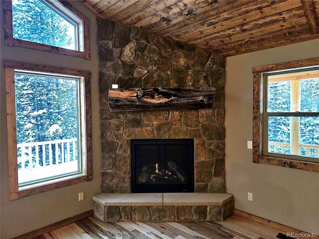 interior space with a stone fireplace, a wealth of natural light, wood ceiling, and wood-type flooring