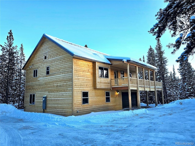 snow covered house featuring a balcony and a garage