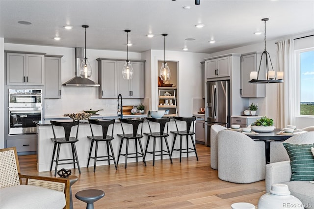 16554 W 93rd Way, Arvada, CO 80007 - kitchen with gray cabinets, appliances with stainless steel finishes, wall chimney exhaust hood, light wood-style floors, and a kitchen bar