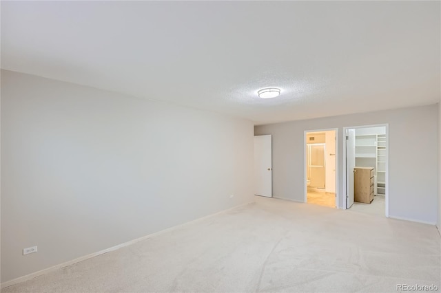 unfurnished bedroom with a textured ceiling, ensuite bath, a walk in closet, a closet, and light colored carpet