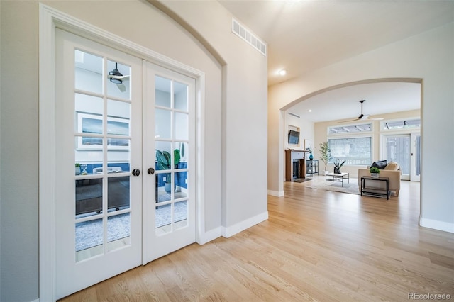 doorway with a fireplace, french doors, arched walkways, wood finished floors, and a ceiling fan