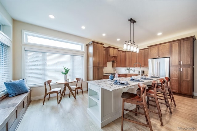 kitchen with open shelves, a kitchen breakfast bar, light wood-type flooring, light stone countertops, and brown cabinetry