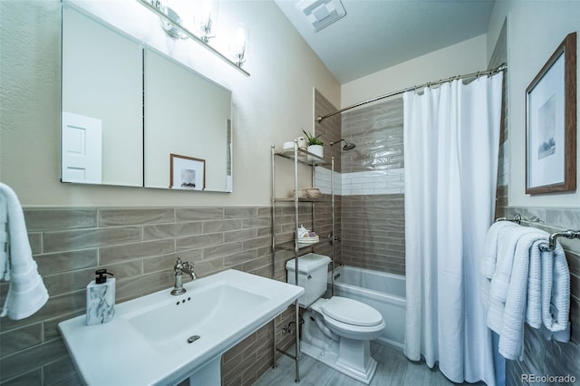 full bathroom featuring tile walls, a sink, shower / tub combo, toilet, and a wainscoted wall
