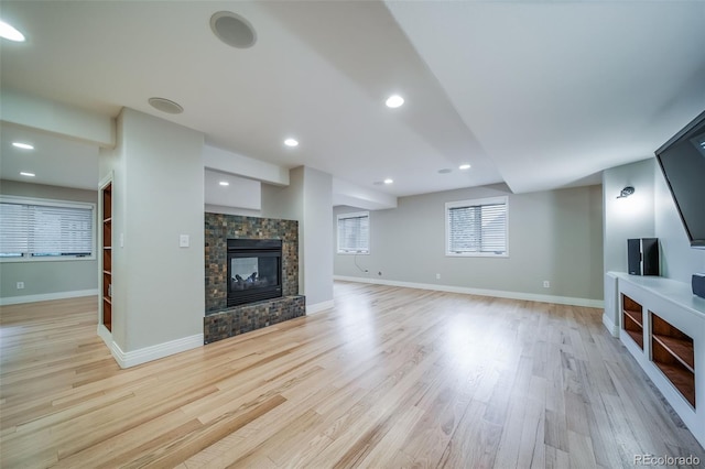unfurnished living room featuring light wood-style floors, a tiled fireplace, and baseboards