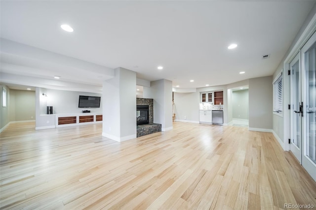 unfurnished living room with a multi sided fireplace, recessed lighting, light wood-style flooring, and baseboards