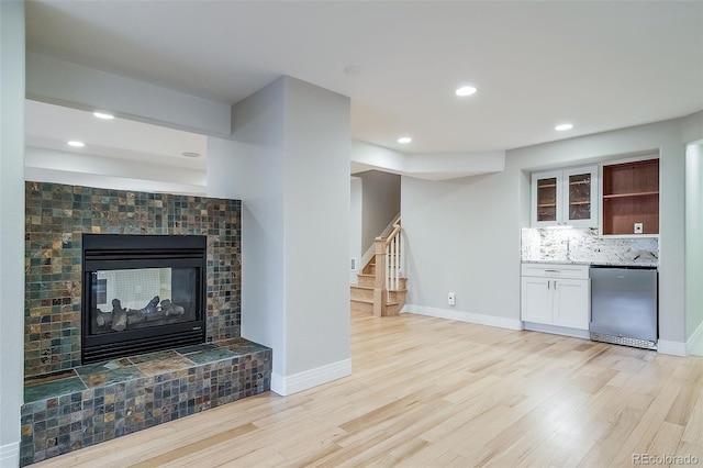 unfurnished living room with light wood-style flooring, stairway, wet bar, a tile fireplace, and recessed lighting