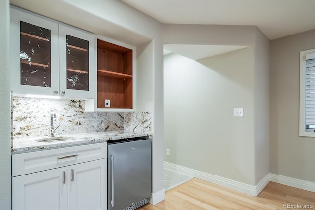 indoor wet bar with stainless steel refrigerator, light wood finished floors, decorative backsplash, and baseboards