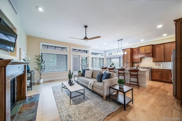 living room with a ceiling fan, light wood-style flooring, a premium fireplace, baseboards, and recessed lighting