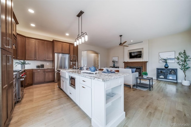 kitchen with stainless steel appliances, a ceiling fan, a fireplace, open shelves, and arched walkways