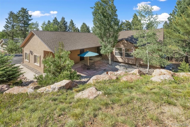 view of front of property featuring stucco siding, a patio, and a shingled roof