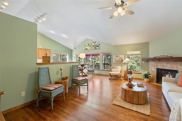 living room featuring a ceiling fan, lofted ceiling, wood finished floors, rail lighting, and a glass covered fireplace