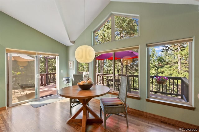dining room with plenty of natural light, wood finished floors, and high vaulted ceiling