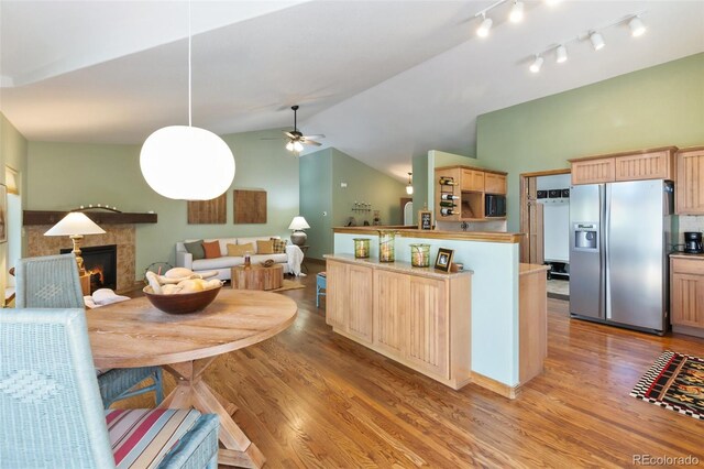 dining room featuring light wood-type flooring, vaulted ceiling, ceiling fan, a warm lit fireplace, and rail lighting