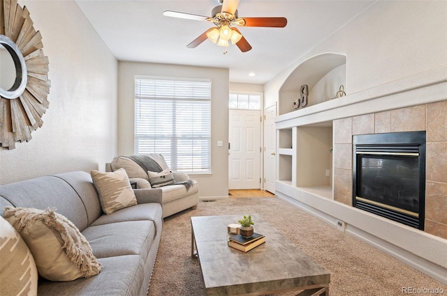 living area featuring carpet floors, a ceiling fan, baseboards, and a tile fireplace