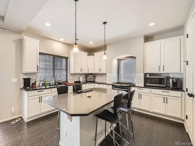 kitchen featuring a breakfast bar, decorative light fixtures, a center island, stainless steel appliances, and white cabinets