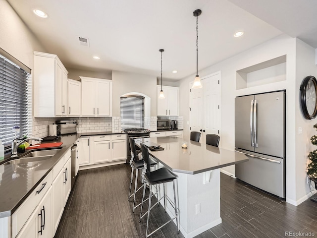 kitchen featuring tasteful backsplash, a kitchen island, pendant lighting, stainless steel appliances, and white cabinets