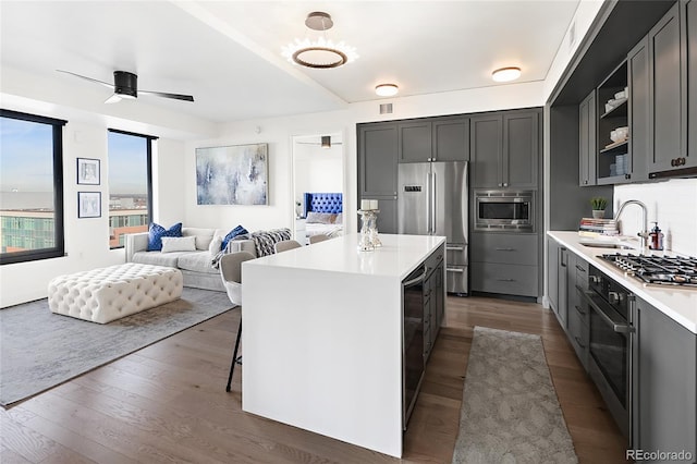 kitchen with sink, dark wood-type flooring, ceiling fan, appliances with stainless steel finishes, and a center island