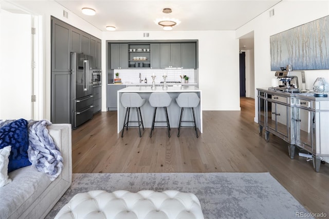 kitchen featuring dark wood-type flooring, stainless steel refrigerator, a breakfast bar, gray cabinetry, and tasteful backsplash