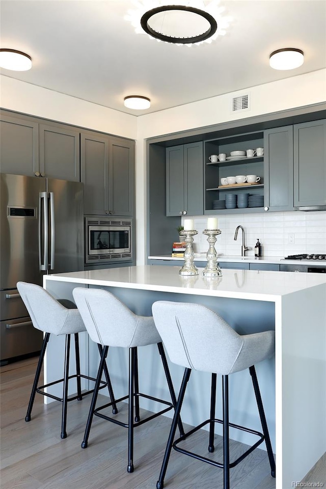 kitchen featuring stainless steel appliances, a breakfast bar area, light wood-type flooring, and decorative backsplash