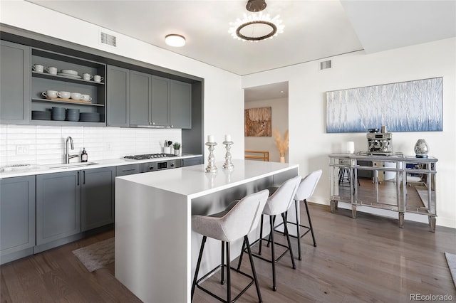 kitchen featuring dark wood-type flooring, sink, a kitchen island, stainless steel gas stovetop, and backsplash