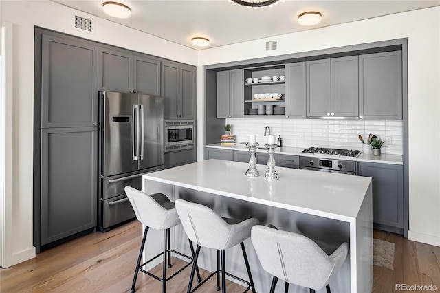 kitchen with tasteful backsplash, a center island, light hardwood / wood-style flooring, gray cabinets, and stainless steel appliances