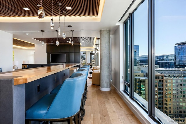 bar featuring a wealth of natural light, wooden counters, a wall of windows, hanging light fixtures, and light wood-type flooring