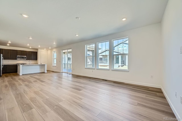 kitchen with stainless steel appliances, light wood-style floors, open floor plan, and light countertops