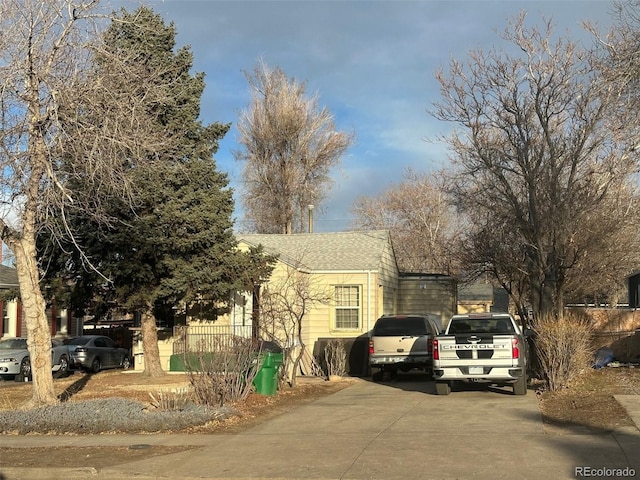 view of front facade with driveway, roof with shingles, and fence