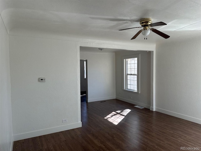 spare room with a textured wall, wood finished floors, a ceiling fan, visible vents, and baseboards