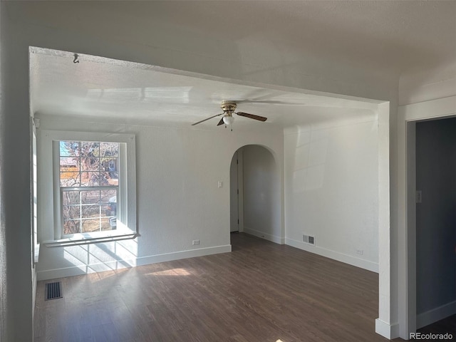 empty room with a ceiling fan, wood finished floors, arched walkways, and visible vents