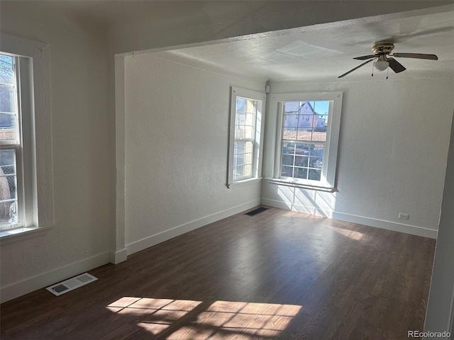 unfurnished room with a wealth of natural light, dark wood-style flooring, and visible vents