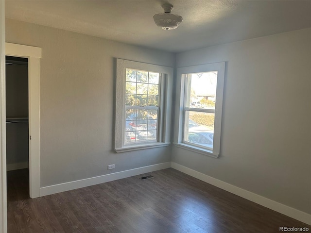 empty room featuring dark wood-type flooring, visible vents, and baseboards