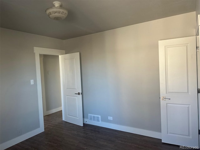 spare room featuring dark wood-type flooring, visible vents, and baseboards