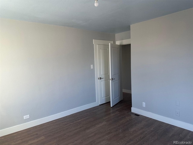 empty room featuring visible vents, dark wood finished floors, and baseboards