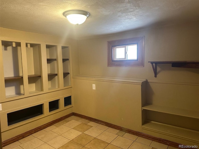 interior space featuring built in shelves, baseboards, a textured ceiling, and light tile patterned flooring