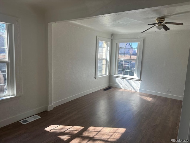 unfurnished room with visible vents, a healthy amount of sunlight, and dark wood-type flooring