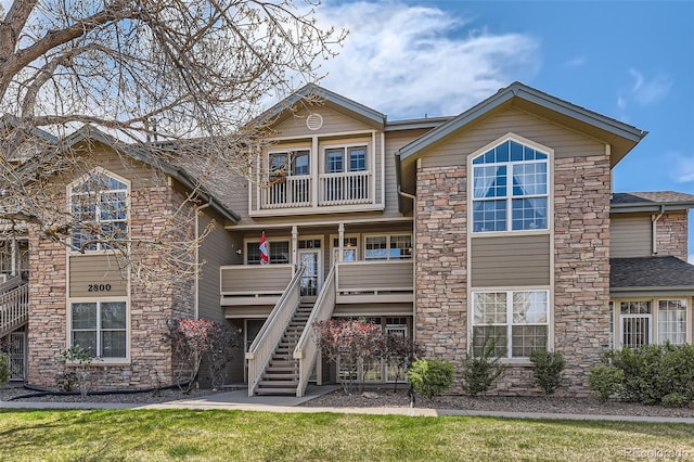 view of front of home with roof with shingles, stairs, stone siding, a balcony, and covered porch