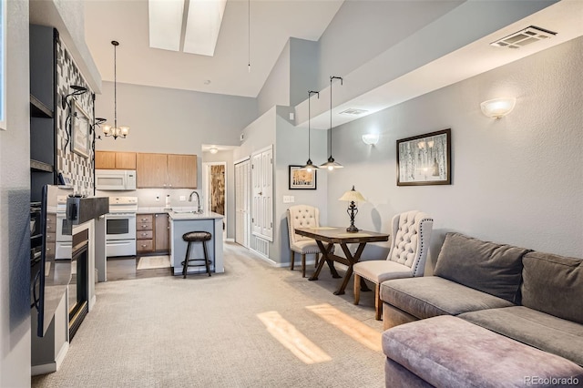 living area featuring visible vents, light carpet, a high ceiling, a chandelier, and a skylight