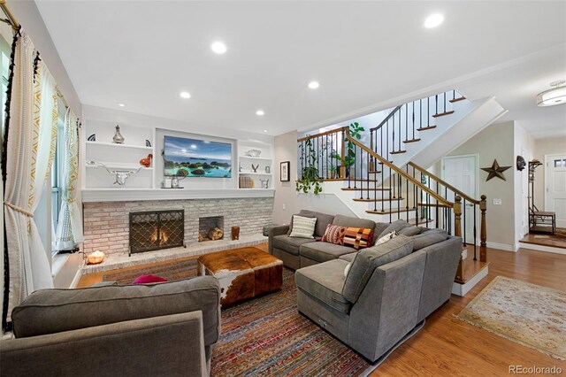 7773 Gunsight Pass, Littleton, CO 80127 - living room featuring stairway, wood finished floors, recessed lighting, baseboards, and a brick fireplace
