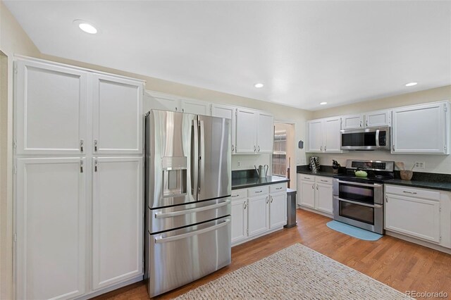 7773 Gunsight Pass, Littleton, CO 80127 - kitchen with appliances with stainless steel finishes, dark countertops, light wood finished floors, white cabinets, and recessed lighting