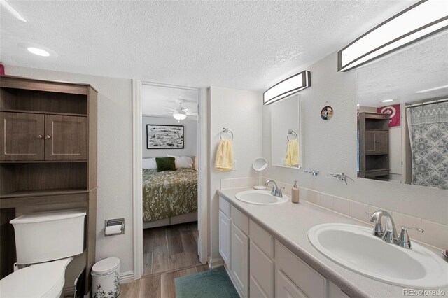 7773 Gunsight Pass, Littleton, CO 80127 - ensuite bathroom featuring a textured ceiling, double vanity, toilet, wood finished floors, and ceiling fan