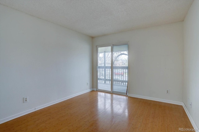 empty room featuring a textured ceiling, wood finished floors, and baseboards