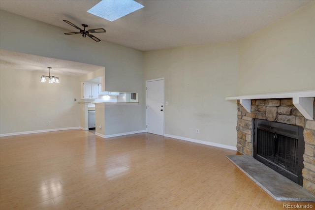 unfurnished living room featuring light wood-style flooring, baseboards, a stone fireplace, ceiling fan with notable chandelier, and a skylight