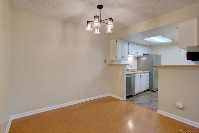 kitchen with a sink, stainless steel appliances, light wood-type flooring, an inviting chandelier, and white cabinetry