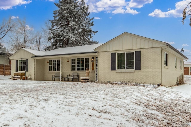 snow covered back of property featuring board and batten siding and brick siding