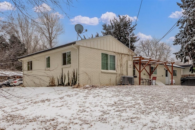 3865 Independence Ct, Wheat Ridge, CO 80033 - view of snowy exterior with board and batten siding, a patio area, brick siding, central AC, and a pergola