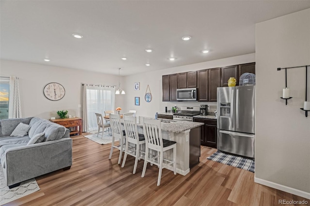 kitchen featuring stainless steel appliances, a kitchen breakfast bar, open floor plan, dark brown cabinets, and light wood finished floors