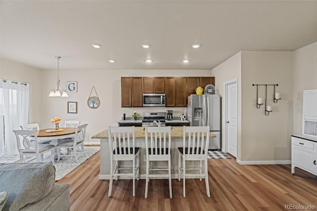 kitchen featuring stainless steel appliances, recessed lighting, an island with sink, wood finished floors, and baseboards