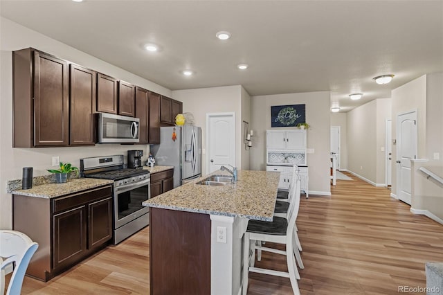 kitchen with a breakfast bar area, stainless steel appliances, light wood-style flooring, a sink, and dark brown cabinetry